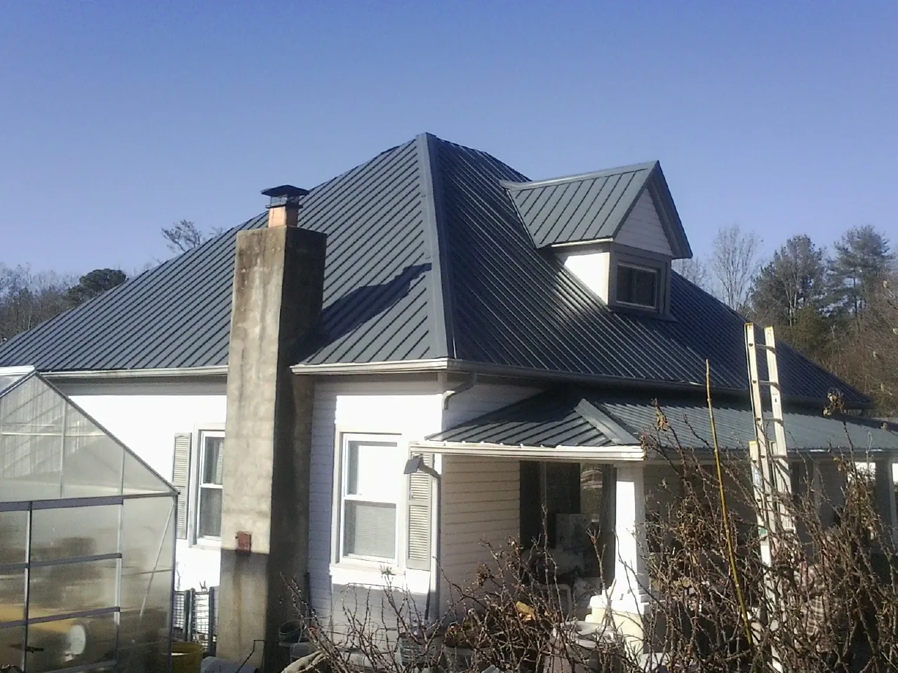 Dark blue standing seam metal roof on a white farmhouse with dormer — Slate & Tile Roof Repair by Roofing Brothers in Toluca