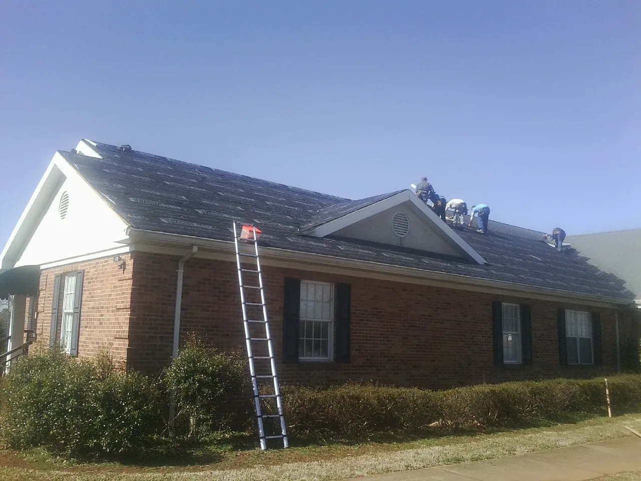 Crew tearing shingles off a brick ranch roof with a ladder set — Emergency Roof Repair work by our crew in Toluca