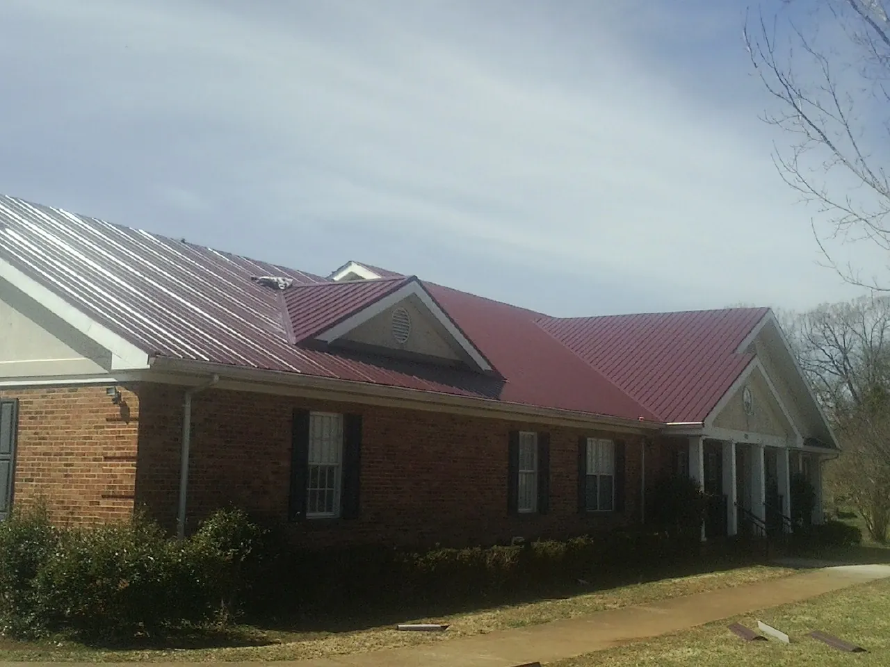 Red metal roof with gabled entries on a long brick building, from a Hail Damage Roof Repair job in Toluca