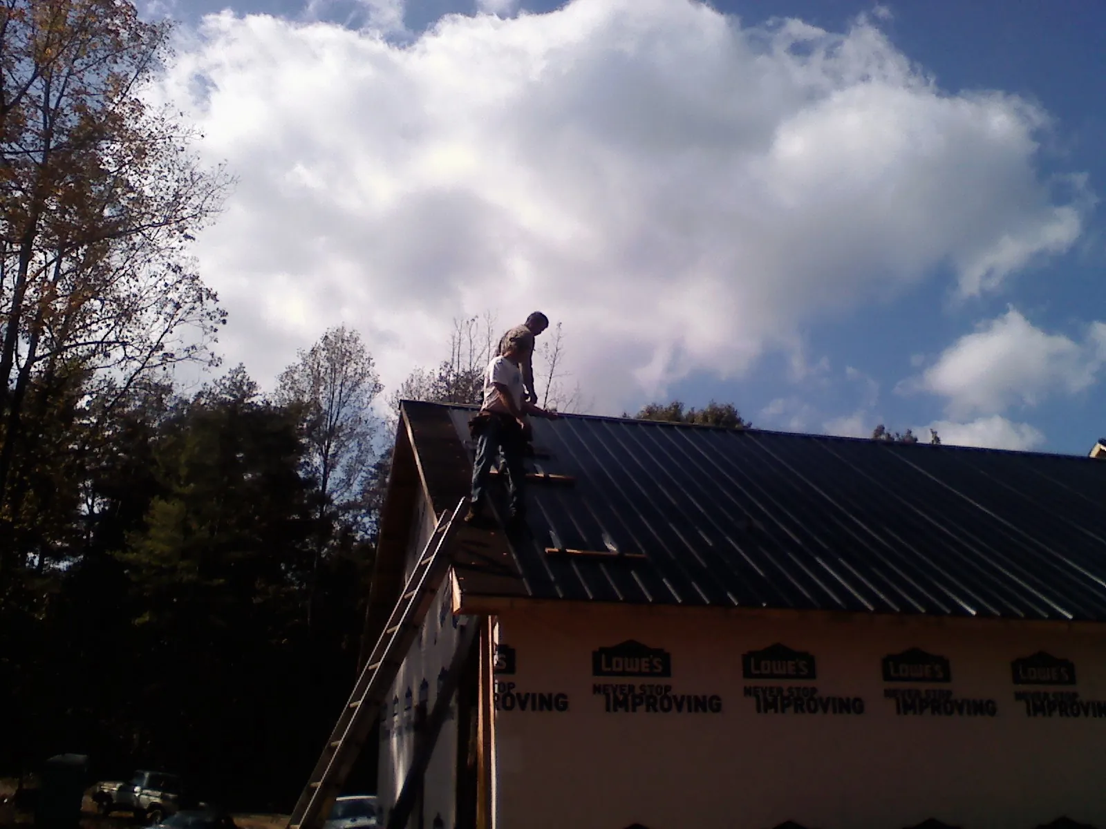 Roofer fastening dark metal panels high against a cloudy sky, from a Roof Inspection job in Toluca