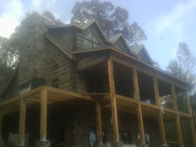 Stone chimney and dormers on a large log home with a timber porch in Toluca