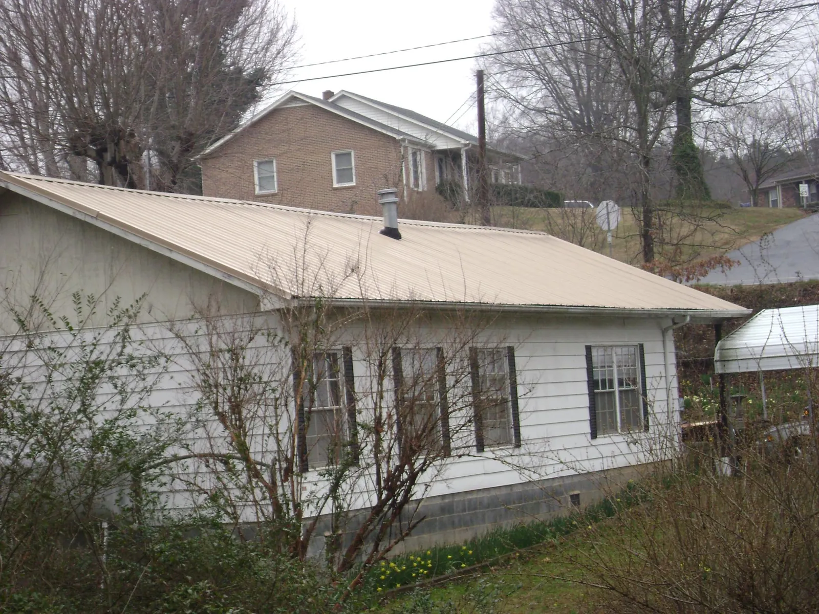 Tan metal roof on a white sided house set into a hillside — Commercial Roofing by Roofing Brothers in Toluca